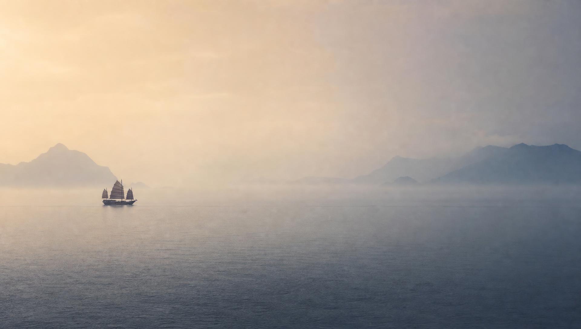 A lone Chinese junk boat sailing through morning haze on a calm sea